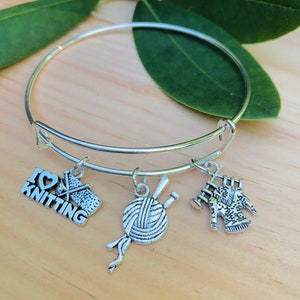Könnte beinhalten: Silbernes Armband mit einem "Ich liebe Stricken"-Anhänger, einem Wollknäuel-Anhänger, einem Stricknadeln-Anhänger und einem Pullover-Anhänger.