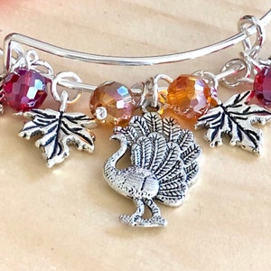 Puede incluir: Pulsera de plata con dijes de temática otoñal, que incluyen un pavo, hojas y cuentas de vidrio rojas y ámbar.