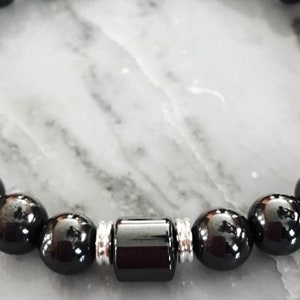 Könnte beinhalten: Ein schwarzes Perlenarmband mit silbernen Akzenten. Das Armband hat eine größere schwarze Perle in der Mitte.