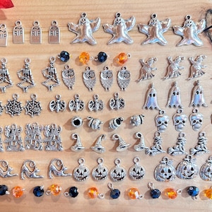May include: A collection of silver Halloween charms, including ghosts, skulls, spiders, bats, pumpkins, and more. There are also some black and orange beads.