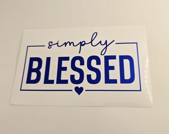 May include: A white sticker with the words "simply BLESSED" in blue. The word "BLESSED" is in bold, capital letters, inside a blue rectangular border. A blue heart is below the word "BLESSED".