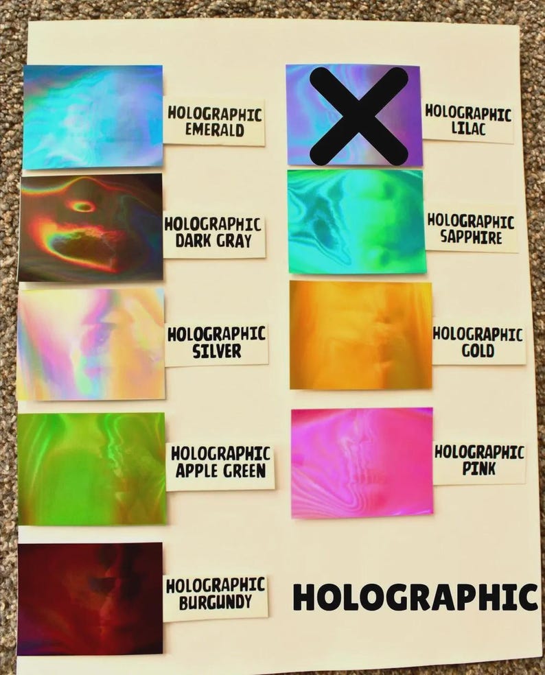 May include: A display of holographic color samples, including emerald, dark gray, silver, apple green, and burgundy. Other colors include lilac, sapphire, gold, and pink. The word "HOLOGRAPHIC" is printed on the bottom right.