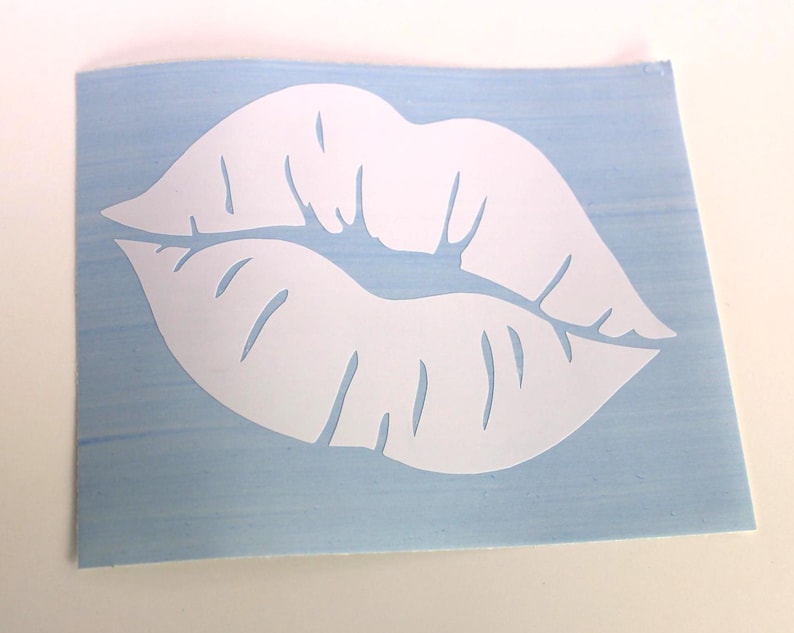 May include: A white lip-shaped decal on a light blue background. The decal is a cut-out of a pair of lips, with details showing the lip lines. The background is a light blue rectangle.