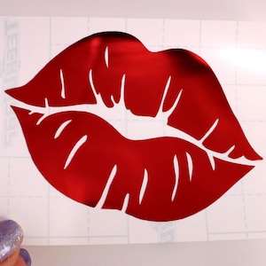 May include: A red, glossy lip decal. The lips are a bold, vibrant red with defined lines and a reflective surface. The decal is on a white background with a grid pattern.
