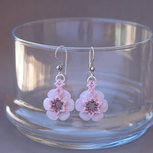 Peut inclure: Une paire de boucles d'oreilles en forme de fleur en perles roses avec des crochets argentés. Les boucles d'oreilles sont délicates et féminines.