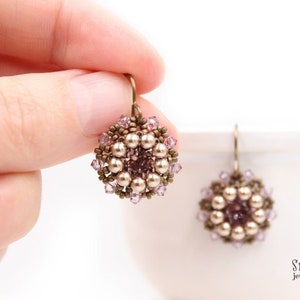 May include: A pair of delicate earrings with a floral design. The earrings are made with small, round, pearl-like beads and tiny pink crystals. The earrings are suspended from a bronze-coloured wire.