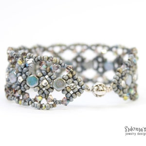 May include: A silver and grey beaded bracelet with a woven design and iridescent accents. The bracelet is made with small seed beads and larger, faceted beads.
