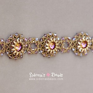 Op de afbeelding: Een gouden kralen armband met roze en paarse accenten. De armband heeft een bloemmotief met een centraal kristal.