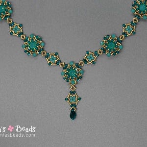 Pu&ograve; includere: Una collana di perline turchese con dettagli dorati. La collana presenta un pendente centrale con una perla a forma di goccia e grappoli floreali. La collana &egrave; esposta su uno sfondo grigio.