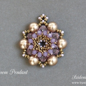 May include: A handcrafted pendant with a floral design. The pendant features large, gold-colored beads and smaller, lavender-colored crystals, arranged around a central cluster. The text "In Blossom Pendant" is visible.