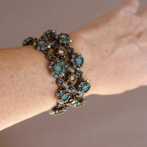 K&ouml;nnte beinhalten: Ein mehrreihiges Armband mit blauen und goldenen Perlen. Das Armband besteht aus kleinen, runden Perlen, die in einem Muster aufgereiht sind. Das Armband wird am Handgelenk getragen.