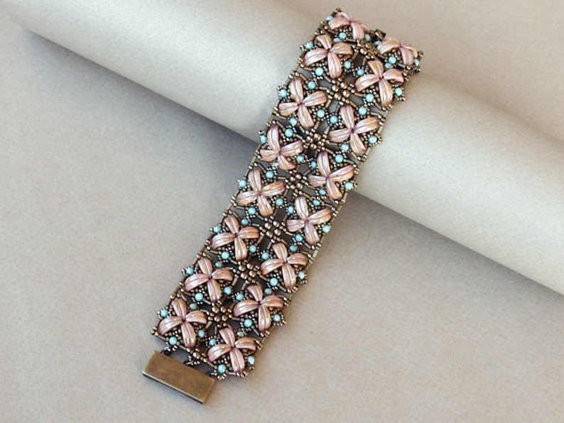 Pu&ograve; includere: Un braccialetto di perline con un delicato motivo floreale. Il braccialetto &egrave; realizzato con piccole perline rosa chiaro e blu, e perline color bronzo. Il braccialetto &egrave; intrecciato in un motivo complesso, creando un design bellissimo e intricato.