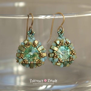 Peut inclure: Une paire de boucles d'oreilles pendantes de forme goutte. Les boucles d'oreilles sont faites de perles vertes et dorées et présentent un cristal transparent au centre.