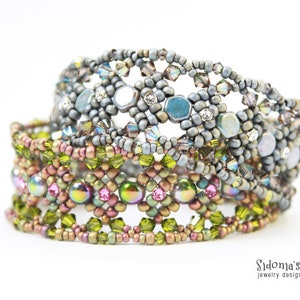 May include: Three beaded bracelets stacked on top of each other. The top bracelet is silver with a geometric pattern. The middle bracelet is brown with a geometric pattern. The bottom bracelet is green with a geometric pattern.