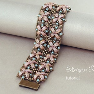 Könnte beinhalten: Ein Armband aus Perlen mit einem rosa-blauen Blumenmuster. Das Armband ist aus kleinen Perlen gefertigt und hat einen Metallverschluss. Das Armband liegt auf einer hellbraunen Oberfläche. Der Text "Stargazer Lilies tutorial" ist im Bild sichtbar.