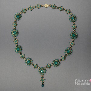 Pu&ograve; includere: Una collana di perline turchese con dettagli color oro. La collana presenta un design floreale con un pendente centrale e una chiusura abbinata. La collana &egrave; esposta su uno sfondo grigio.