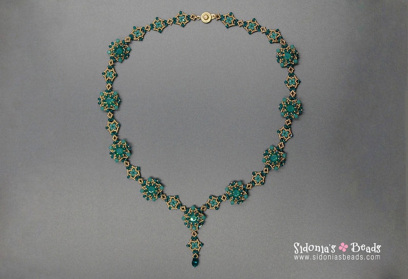 Pu&ograve; includere: Una collana di perline turchese con dettagli color oro. La collana presenta un design floreale con un pendente centrale e una chiusura abbinata. La collana &egrave; esposta su uno sfondo grigio.