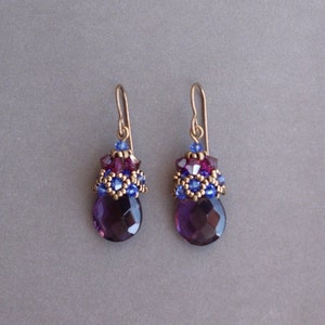 Op de afbeelding: Paarse edelsteen oorhangers met goudkleurige metalen accenten en blauwe en paarse kralen.