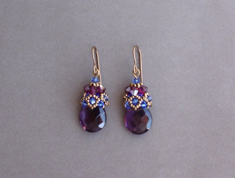 Op de afbeelding: Paarse edelsteen oorhangers met goudkleurige metalen accenten en blauwe en paarse kralen.