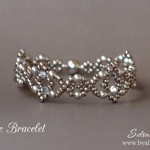 May include: A silver and white beaded bracelet with a geometric design. The bracelet is called "Losange Bracelet" and is by Sidonia Petki.