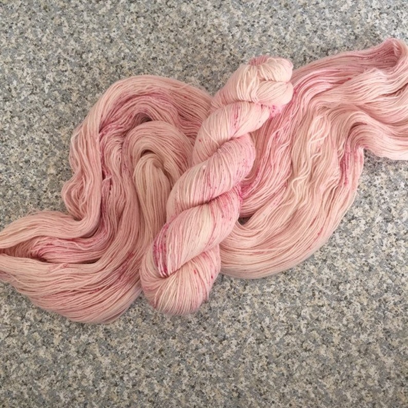 May include: A skein of hand-dyed yarn in shades of pink and rose. The yarn is loosely wound, with a soft, textured appearance. The color is a blend of light and dark pinks, with subtle variations throughout. This yarn is suitable for knitting and crochet projects.
