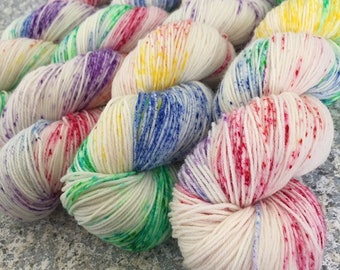 Puede incluir: Primer plano de una madeja de hilo blanco con motas de colores rojo, amarillo, azul, verde y morado. El hilo está dispuesto en una serie de bucles.