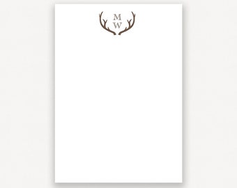 May include: A white notepad with a brown antler design and the initials "M W" in gray text.