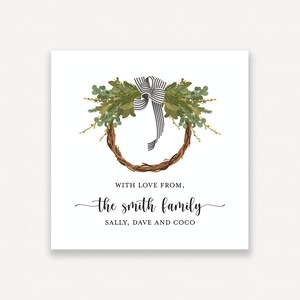 May include: A white card with a green and brown wreath with a black and white ribbon. The text "With love from, the smith family, Sally, Dave and Coco" is printed below the wreath.