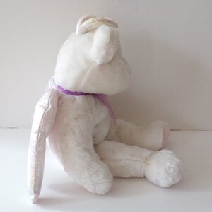 Peut inclure: Ours en peluche blanc en forme d'ange avec un ruban violet et des ailes iris&eacute;es.