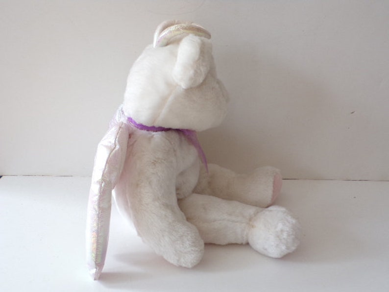 Peut inclure: Ours en peluche blanc en forme d'ange avec un ruban violet et des ailes iris&eacute;es.