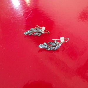 May include: A pair of silver earrings shaped like a leaf with clear rhinestones.