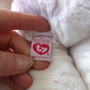 Peut inclure: Peluche blanche et violette avec une &eacute;tiquette Ty rouge qui indique "The Beanie Buddies Collection" et "Shell 100% Nylon".