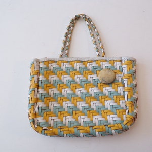 May include: A small, woven handbag with a white, yellow, and blue geometric pattern. The bag has a single top handle and a button closure.