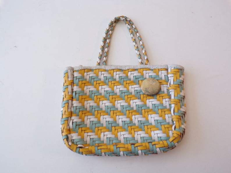 May include: A small, woven handbag with a white, yellow, and blue geometric pattern. The bag has a single top handle and a button closure.
