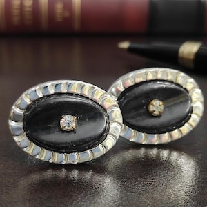 May include: A white ceramic mug with a black handle and the text "But First, Coffee" in a bold, black font. The mug is set against a blurred background, suggesting a cosy setting.