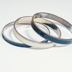 May include: Three silver bangle bracelets with a white and dark blue enamel design.