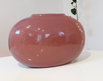 May include: A large, oval-shaped vase with a glossy, dusty rose finish. The vase is sitting on a white surface.