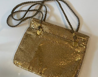 May include: A gold mesh chain bag with a braided brown strap. The bag has a flap closure with a gold clasp.