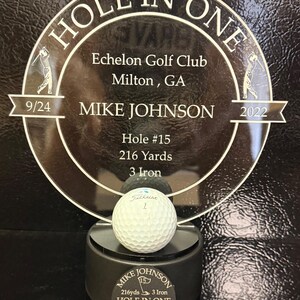 May include: A gold-colored plaque with a golf ball on top. The plaque reads "Hole in One" with the date "9/24/2022" and the name "Mike Johnson". It also states "Echelon Golf Club, Milton, GA" and "Hole #15, 216 Yards, 3 Iron".