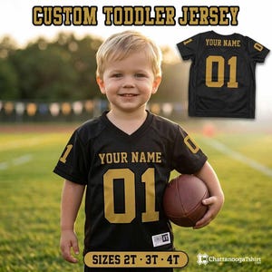 May include: A black toddler jersey with gold lettering and numbers. The front features the text 'YOUR NAME' above the number '01'. The sleeves have the number '01' printed on them. The text 'CUSTOM TODDLER JERSEY' and 'SIZES 2T - 3T - 4T' appear.