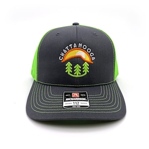 May include: A charcoal gray trucker hat with a neon green mesh back and brim stitching. The front features an embroidered design with the word "Chattanooga" above a sun and tree graphic. The hat includes a Richardson 112 tag.
