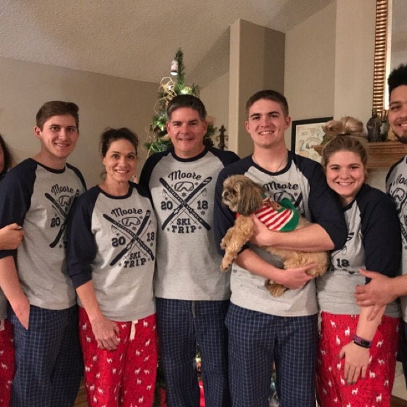 May include: A family of five wearing matching gray and navy blue shirts with the text "Moore 2018 Ski Trip" and a ski graphic. The family is standing in front of a Christmas tree and holding a small brown dog.