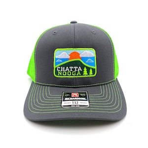 May include: A gray and green trucker hat with a patch that says "Chattanooga" and features a sunset and trees. The hat is made by Richardson and has a size tag that says "112".