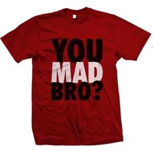 Puede incluir: Camiseta roja con el texto "YOU MAD BRO?" en letras negras y blancas.