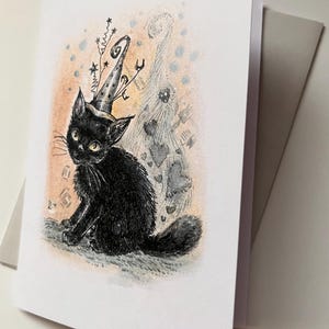 May include: A greeting card featuring a black cat wearing a wizard hat with star and swirl accents. The cat is sitting, with a whimsical background of hearts and dots. The card is white with a gray envelope.