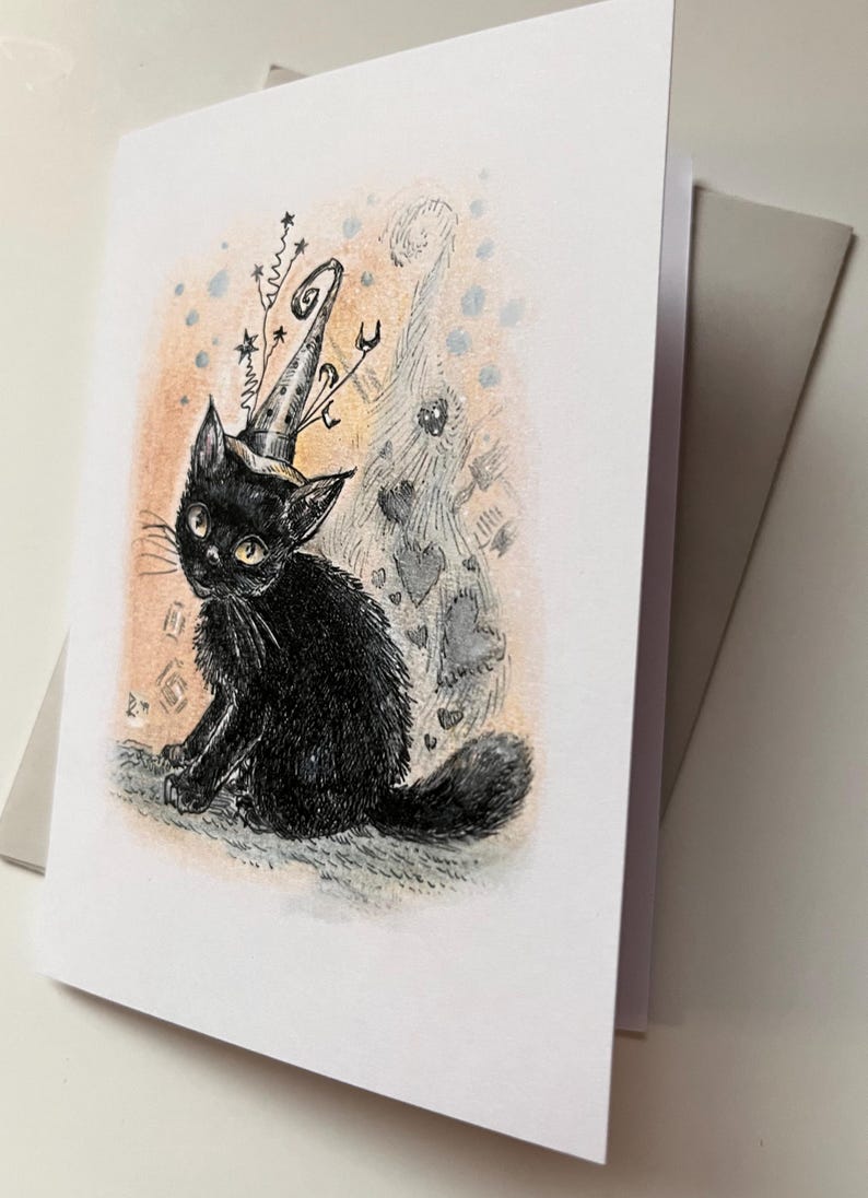 May include: A greeting card featuring a black cat wearing a wizard hat with star and swirl accents. The cat is sitting, with a whimsical background of hearts and dots. The card is white with a gray envelope.
