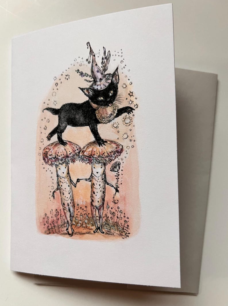 May include: Greeting card featuring a whimsical illustration. A black cat wearing a hat and collar stands atop two mushroom-headed figures. The card has a light pink and white background with a gray envelope.