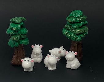 May include: A miniature pastoral scene featuring five white sheep figurines with pink ears and noses, positioned around two green and brown tree figurines. The sheep are in various poses, creating a charming, whimsical display.