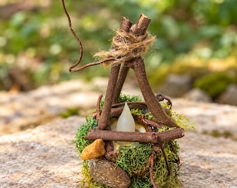 May include: A decorative structure made of brown twigs tied with twine, featuring a base covered in green moss and small stones. A white, flame-shaped LED light sits in the center of the twig frame, which includes a curved vine accent.