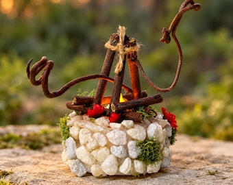 May include: A decorative candle holder shaped like a miniature campfire, featuring a base covered in white stones and green moss, with brown twigs arranged in a teepee structure tied with twine and accented by small red flowers.